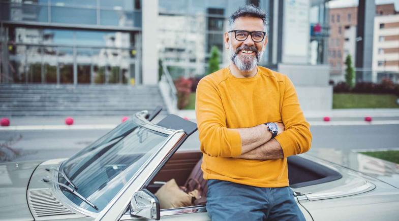 Älterer Mann lehnt in einer Großstadt an seinem Oldtimer-Cabrio