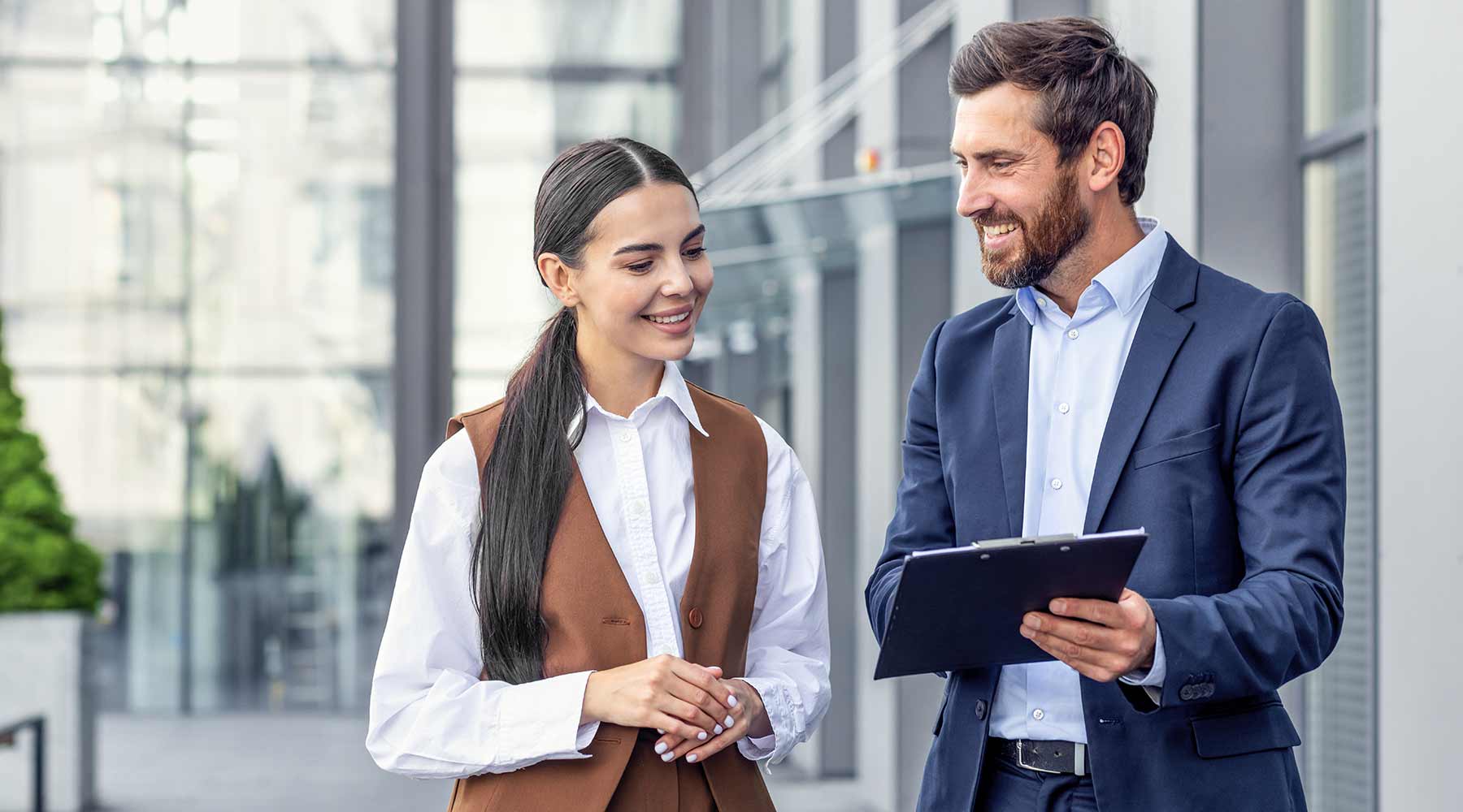 Mann und Frau in Business-Kleidung schauen außerhalb eines Bürogebäudes auf ein Tablet.