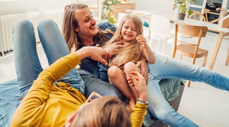 Familie sitzt mit ihrer kleinen Tochter auf der Couch und macht Quatsch