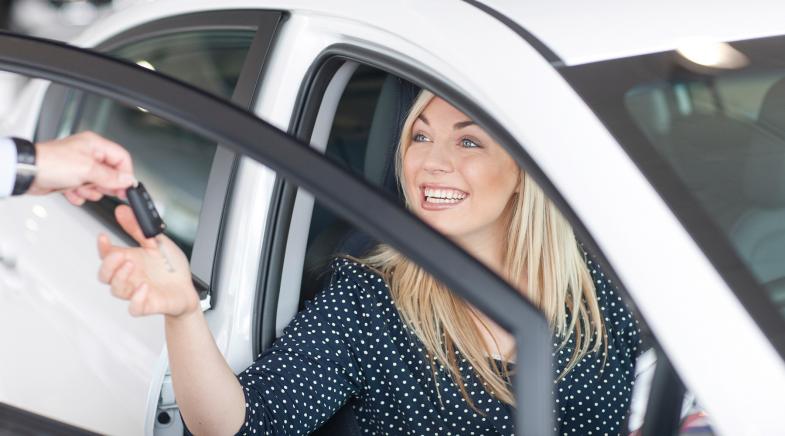 Frau nimmt im Auto sitzend bei offener Tür einen Autoschlüssel entgegen.