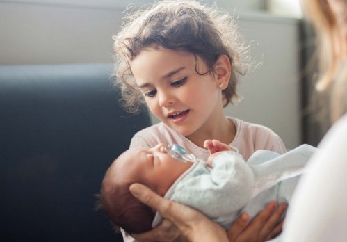 Kleines Mädchen sitzt im Krankenhaus und hält ein Baby im Arm.