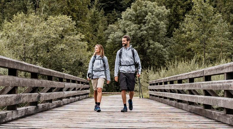 Ein Paar in Funktionsjacken wandert über eine Holzbrücke , die einen Fluss überspannt.