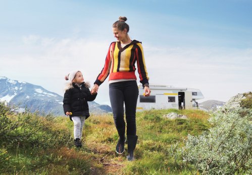 Mutter geht mit Tochter in den Bergen spazieren. Hinter ihnen steht ein Wohnmobil.