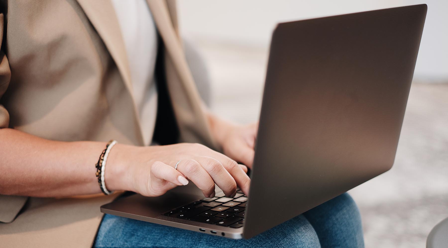 Laptop auf dem Schoß einer Frau in Jeans und Sakko