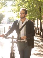 Ein Mann schiebt ein Fahrrad über einen Gehweg zwischen zwei Straßen in einer Stadt.