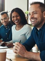 Vier Kollegen und Kolleginnen sitzen lachend in einem Geschäftsmeeting.