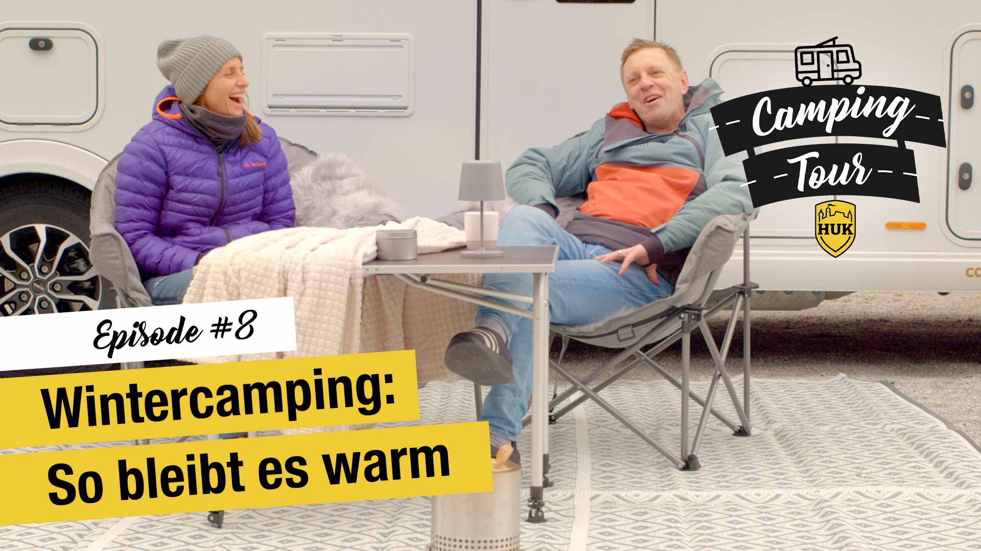 2 warm angezogene Menschen in ihren Campingstühlen vor einem Camper